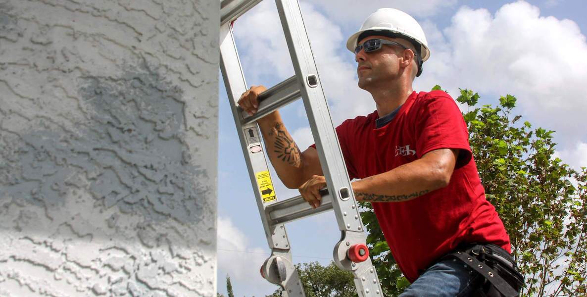 A contractor climbs on a roof to repair a home