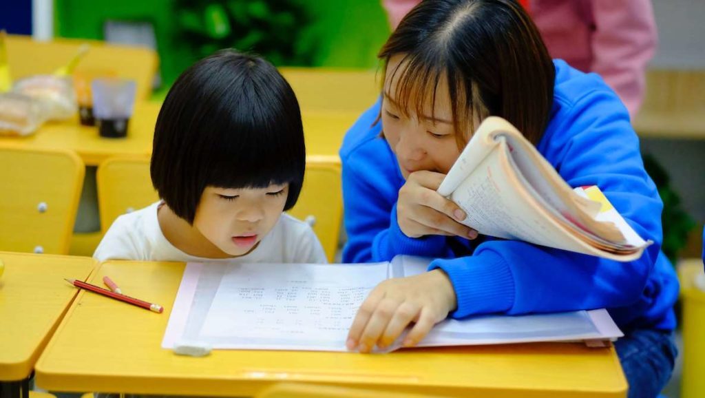 A woman teaches a young girl how to read.