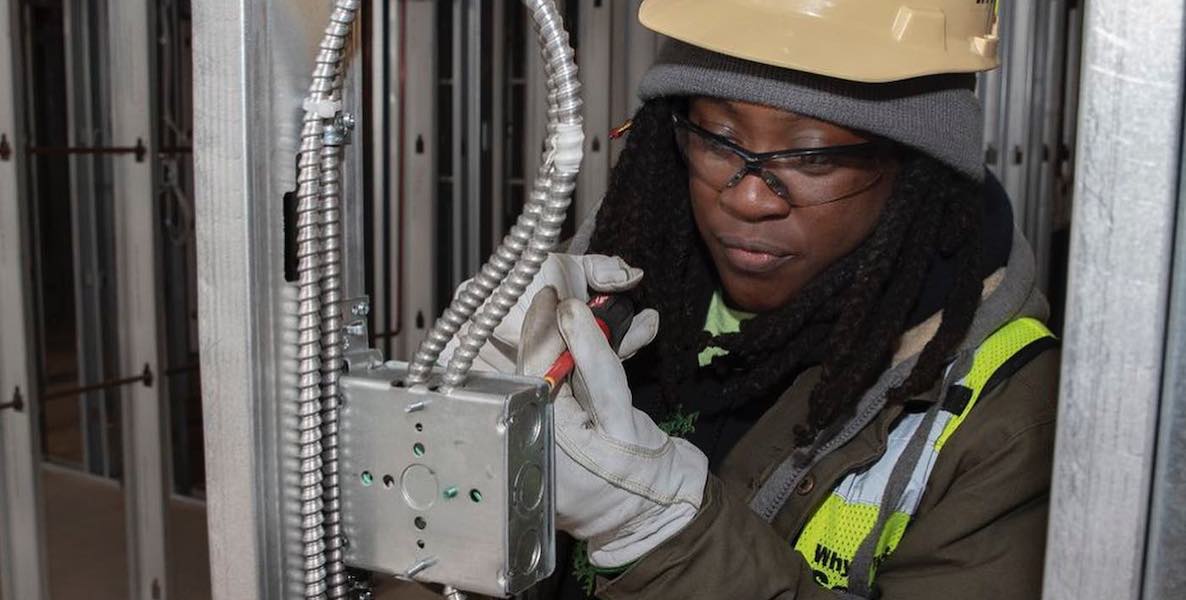 A woman wearing a hard hat, an employee of Post Brothers in Philadelphia, does some electrical work on a development project.