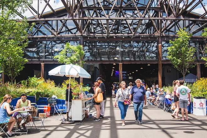 Inside of restored municipal pier in Philadelphia, people walk and sit among plants and cafe tables.