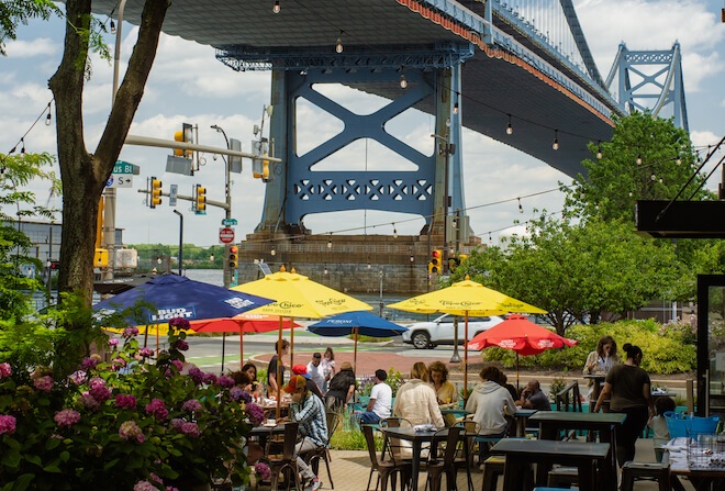 With the Ben Franklin Bridge in the background, the outdoor Haas Biergarten at Fringe Bar shows its umbrellas and tables of patrons.