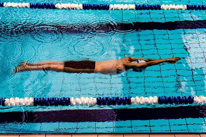 A swimmer in black pro trunks and a white cap glides between rows in a pool
