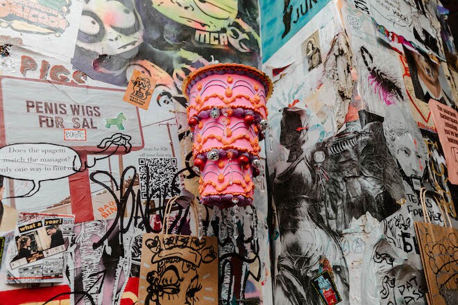 A three-tier pink cake sculpture hangs in the corner of a stickered wall at Tattooed Mom.
