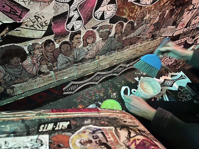 A cutout wheatpaste of iconic women — including Ruth Bader Ginsberg — hangs on a wall at Tattooed Mom. Also in view, an artist's hand and their brush and wheatpaste.