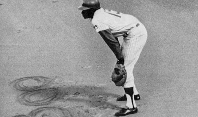 A 1969 photo of Phillies infielder Dick Allen, leaning over with his glove on his left hand. He's traced "BOO" in the dirt, a response to the taunts Phillies spectators hurled at him, despite his stats and skills. 