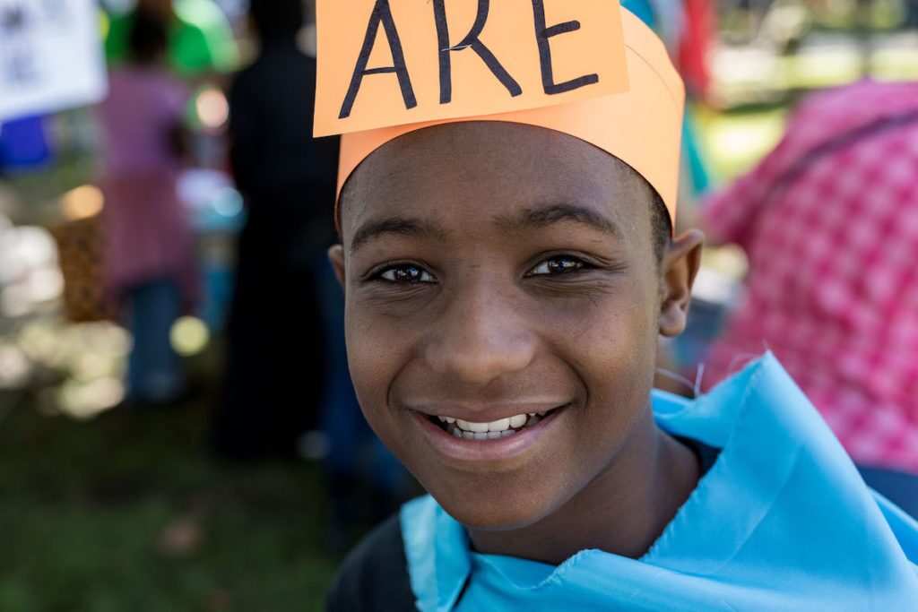 A kid attends Mighty Writers writing festival, wearing a sign on his head that says, "Are."