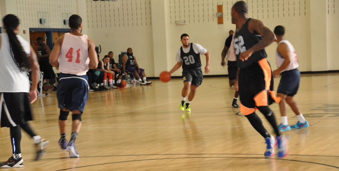 Men play basketball in a gymnasium—one runs down the middle of the court with the ball.