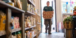 A small business owner carries merchandise into his grocery after it reopens following the coronavirus pandemic