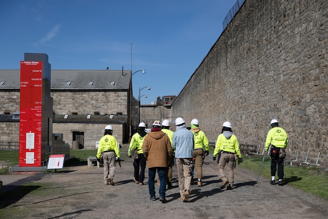 Construction academy professor Chris Capaldi (in a brown work coat, jeans and white hard hat) leads his students back to the classroom.
