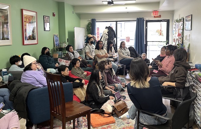 High school and college students sit inside the Ginger Arts Center in a circle, watching one student speak.