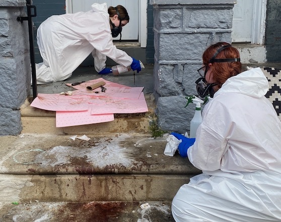 Employees of Trauma Services, a biohazard removal company, wearing hazmat suits, clean blood from steps.