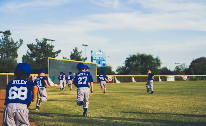 Little children wearing blue shirts with their first names and numbers on the back, elastic-waist baseball pants and caps run on a field.