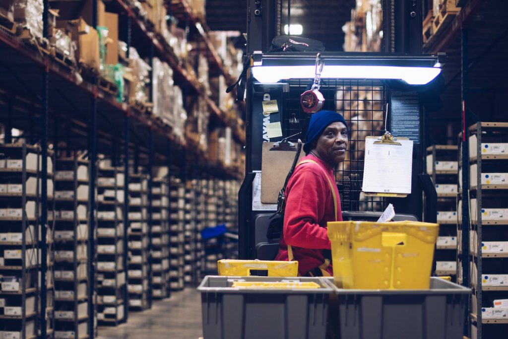 A man in a red shirt and blue beanie puts in work at a factory—a job he secured through First Step Staffing