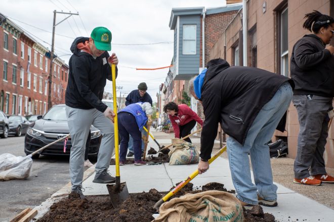 Volunteers prep a square of city sidewalk for a new tree.