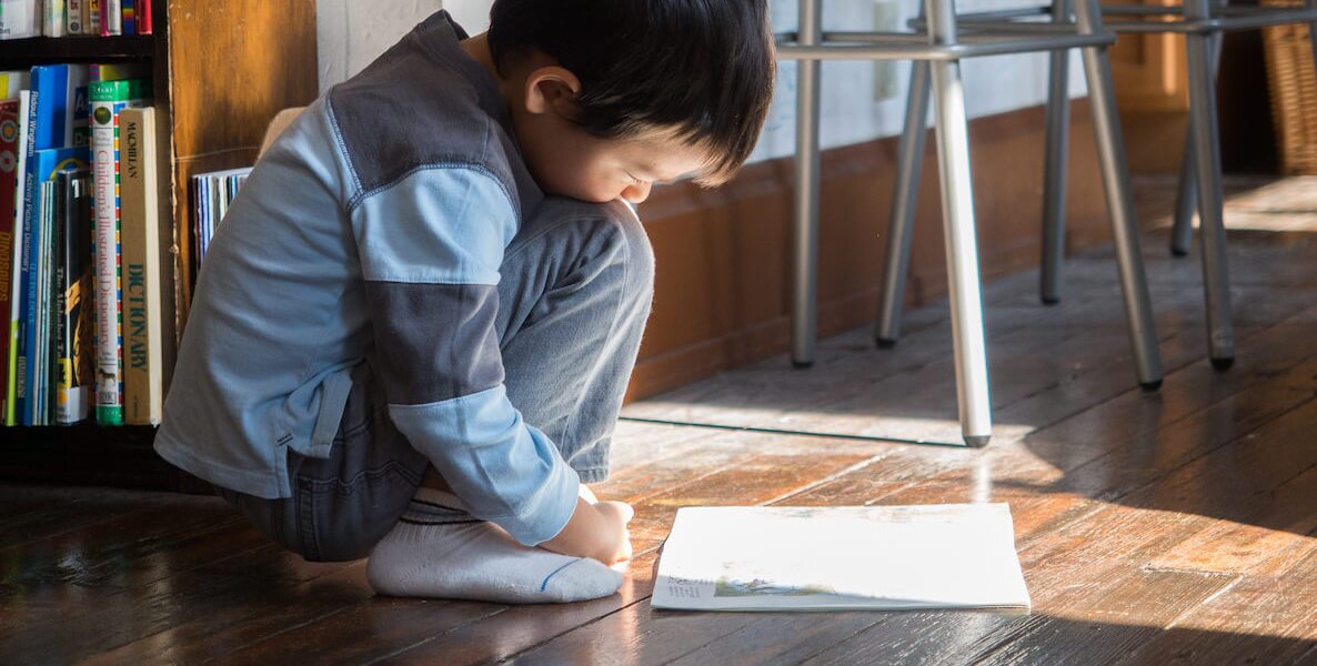 A little boy reads in a sliver of sunshine coming through his living room window during the coronavirus pandemic. Keeping kids engaged with text is one key to avoiding the Covid slide during the pandemic.