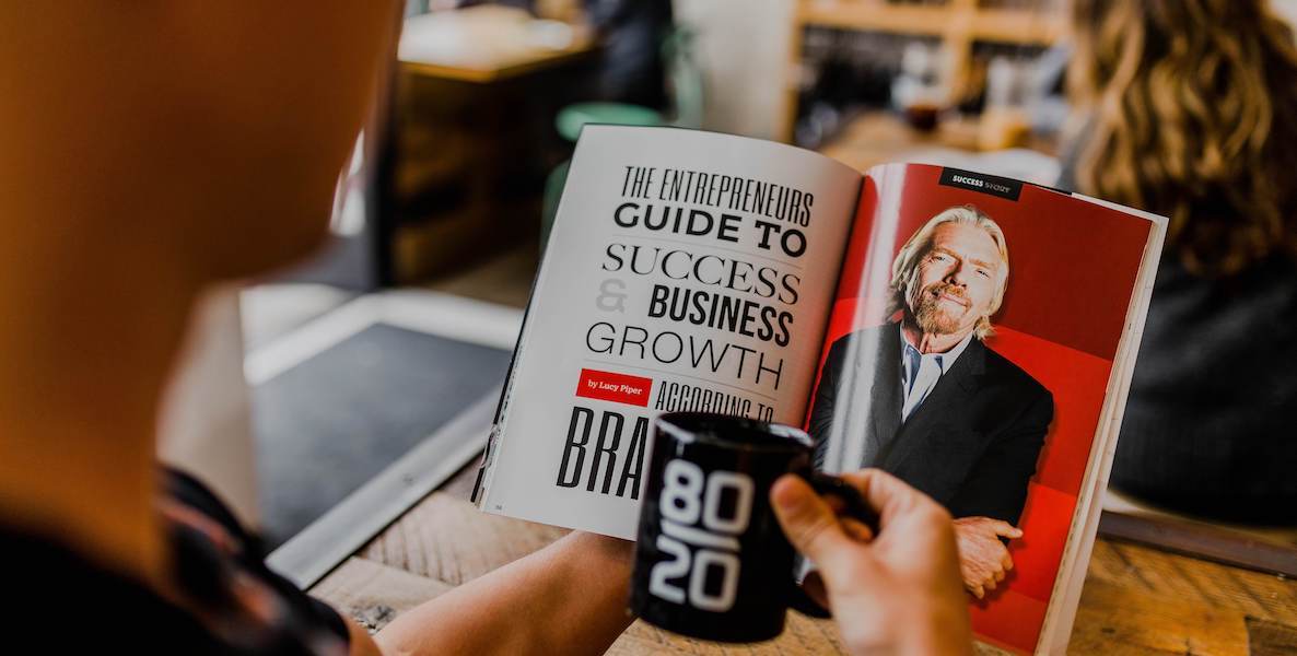 An aspiring entrepreneur reads a magazine article about starting his own business while he sips on a cup of coffee.