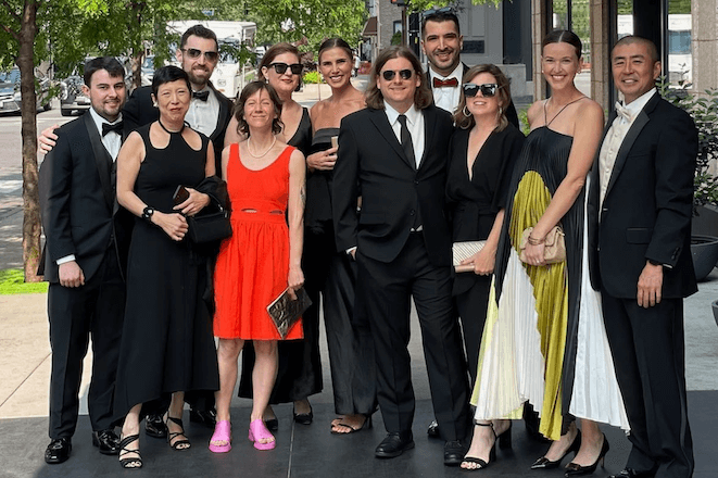A group of people in formal attire stand outside a. kitchen + a. bar on Rittenhouse Square in Philadelphia.