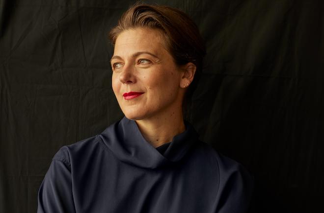 Portrait of Philadelphia Museum of Art Director Sasha Suda, a White woman with brown hair pulled back, red lipstick and a navy top with a cowl neck.
