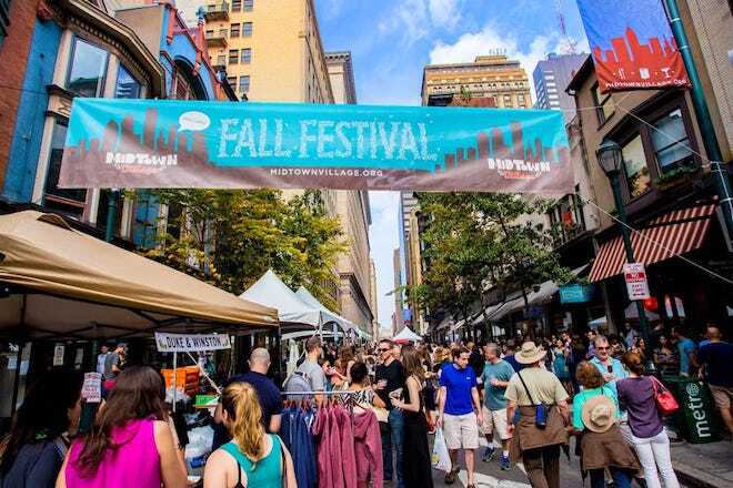 People walk along a pedestrianized 13th Street beneath a banner that reads "midtown village fall festival."