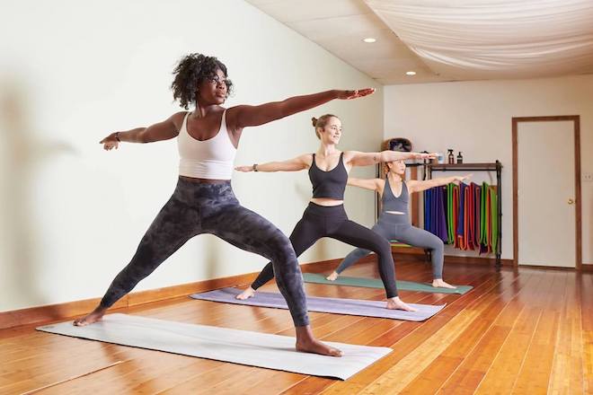 Three women stand side by side in warrior two pose.