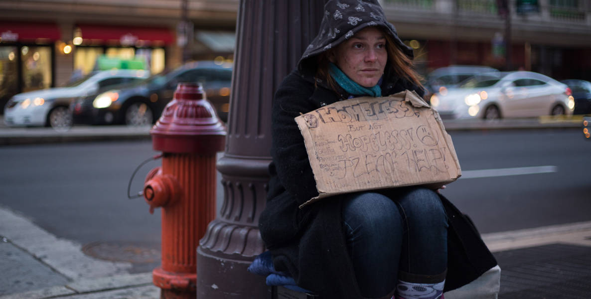 A homeless and hungry woman holds a sign.