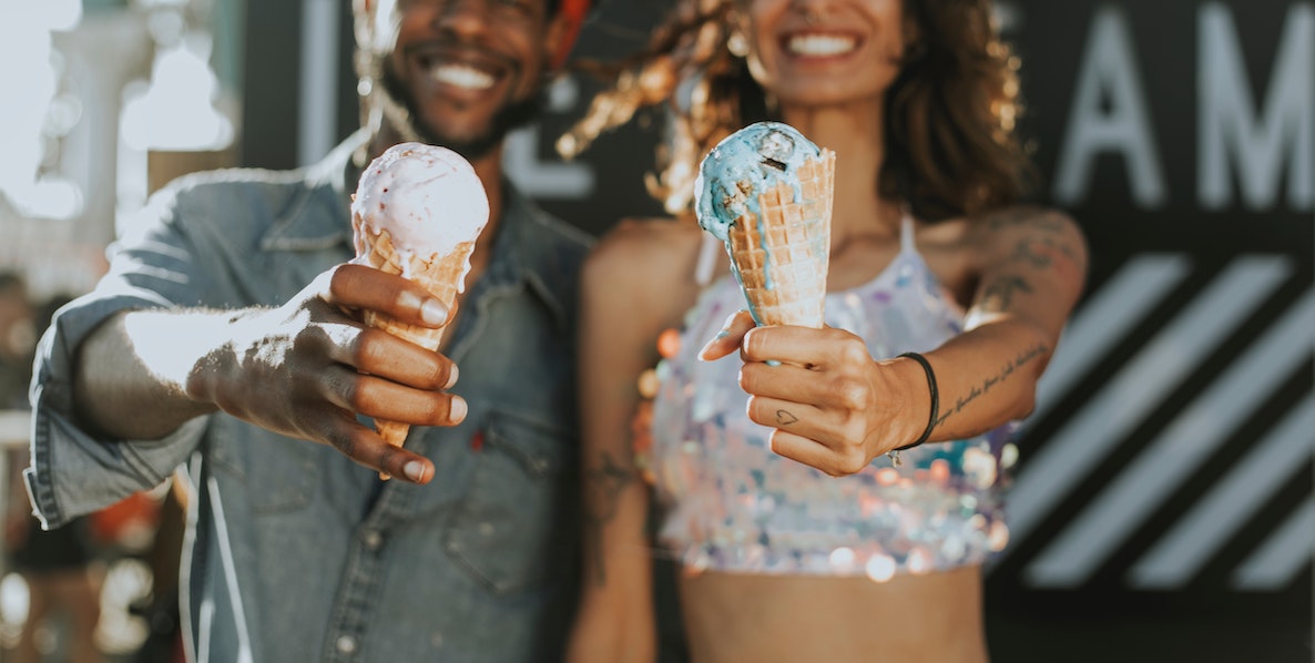 A black couple hold ice creams toward the camera, smiling