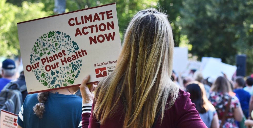 A young woman holds a sign that reads "climate action now."
