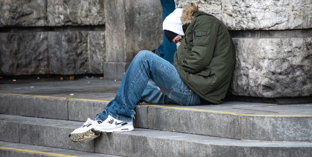 A homeless man curls up on a concrete stoop. Here, a guide to how to help the homeless in Philadelphia.