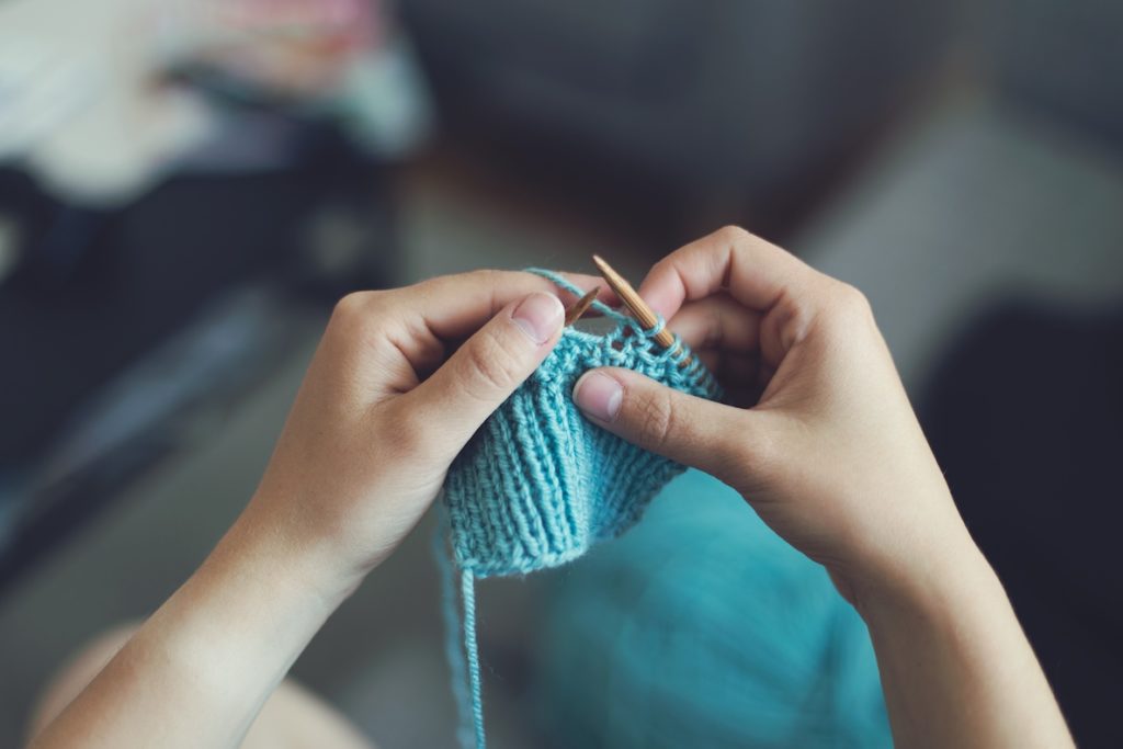 A woman knits a blue sleeve that will eventually become a shirt