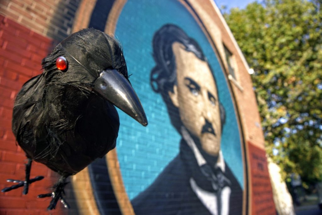 A fake raven looks on as an image of Edgar Allen Poe hovers in the background.