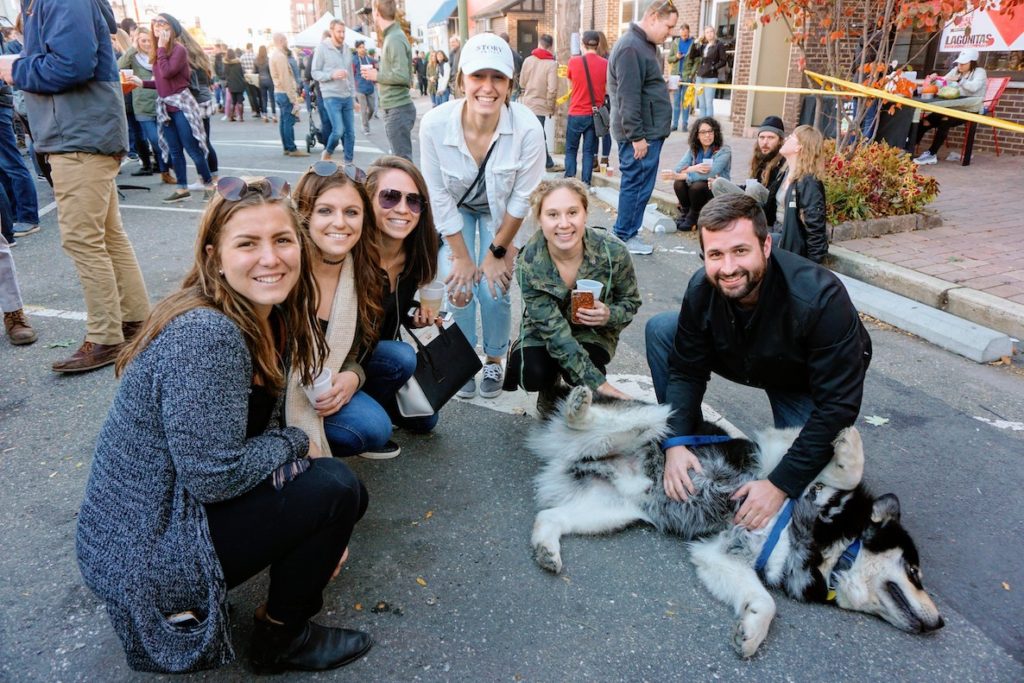 A group of friends huddle around a dog laying on the street at the annual Great Harvest Cider and Beer Festival at Hawthornes/