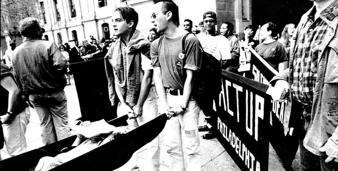 Two young ACT UP protestors carry a pretend dead body to protest the government's response to AIDS in the 1990s.