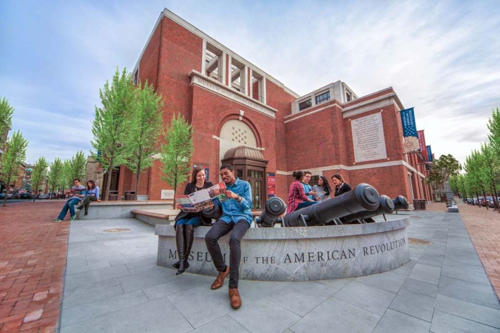 Two people sit on a wall outside the Museum of the American Revolution reading a map.