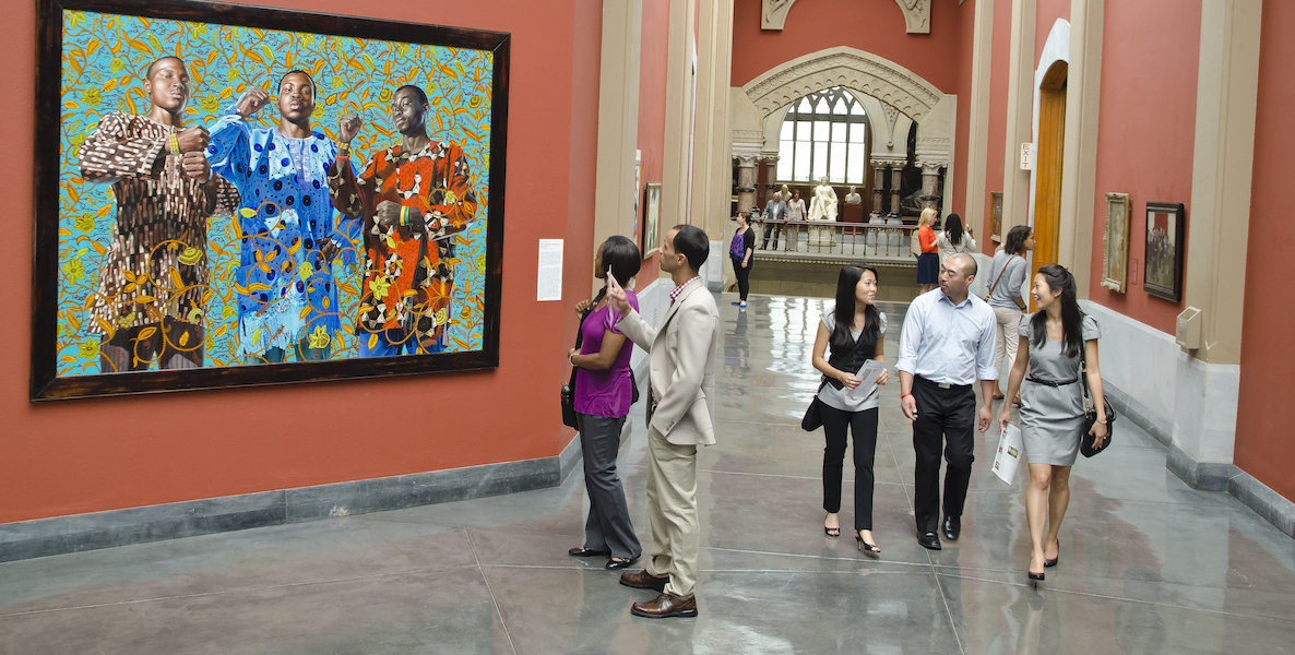 Museum goers check out an artwork showing three colorfully dressed black men at the Pennsylvania Academy of the Fine Arts, or PAFA