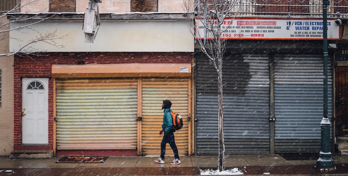 Man walks down the streets of Philadelphia, with shuttered stores in the background