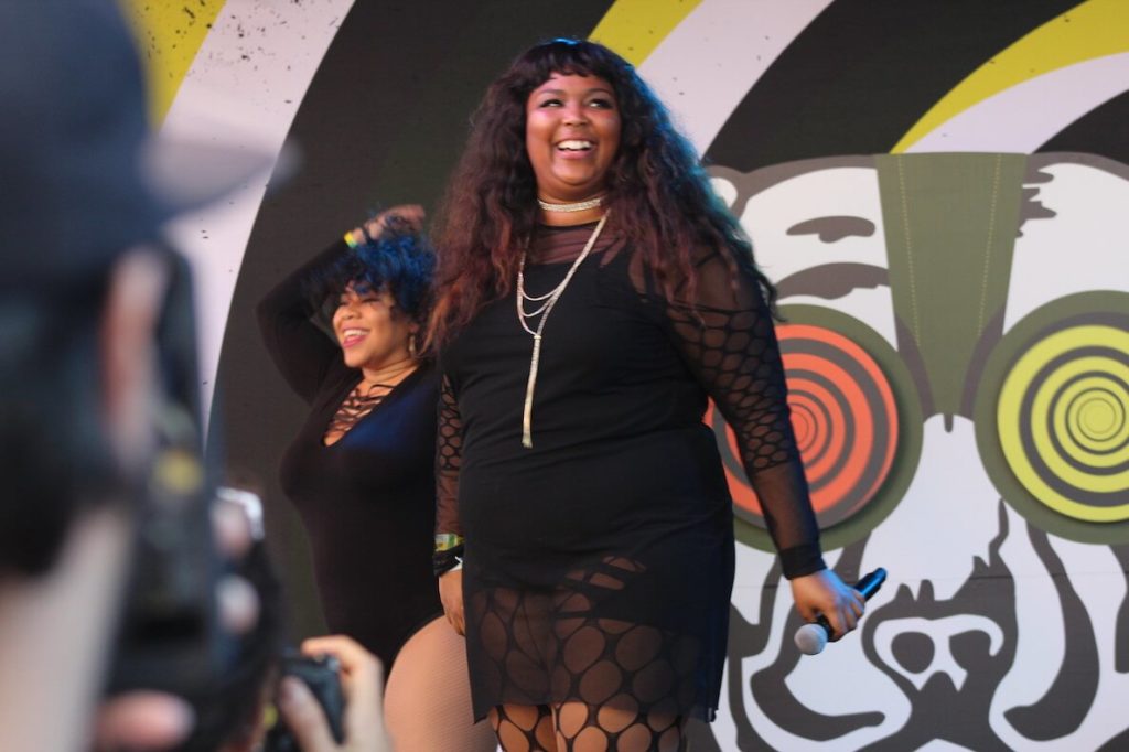 Lizzo stands on stage with a big ol' smile spread across her beautiful face.