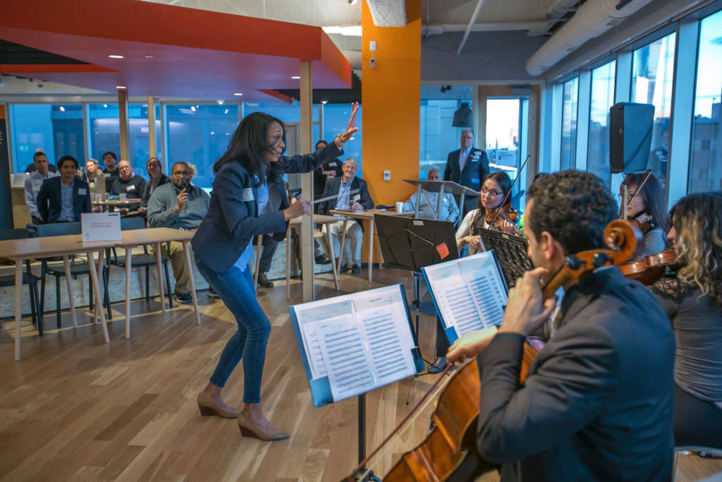 A woman conducts a band at Venture Cafe Philadelphia, which offers entertainment aspects at its weekly meetings.