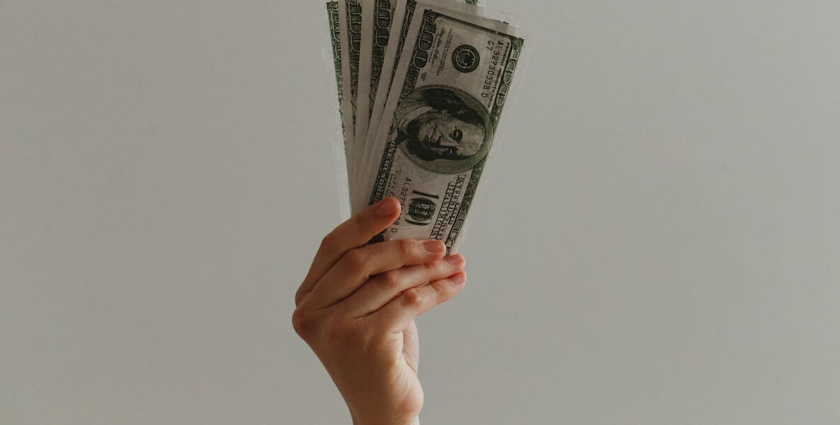 A single hand holds up several one-hundred-dollar bills.