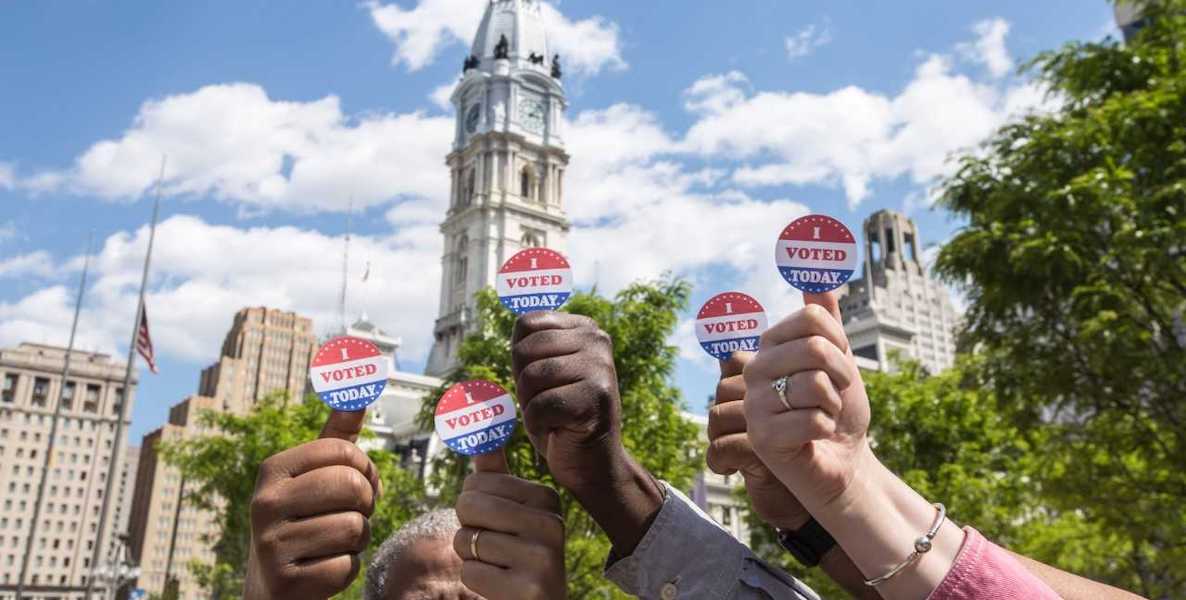Philadelphia voters hold voting stickers up in the air in front of Philadelphia City Hall.