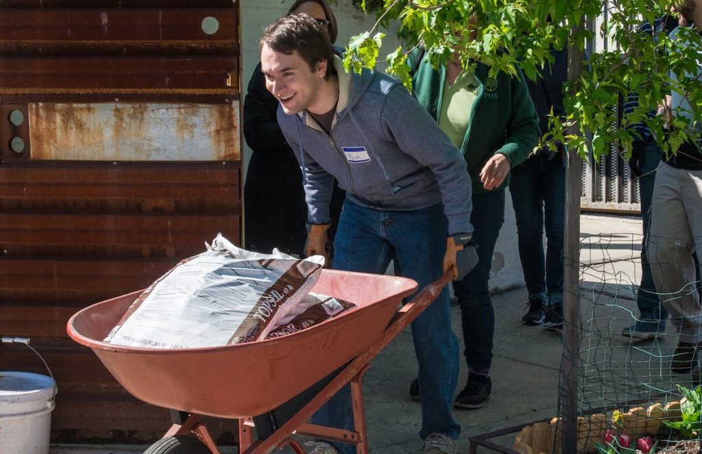 A volunteer pushes a wheel barrel into a vacant lot to spruce it up and plant some things. 
