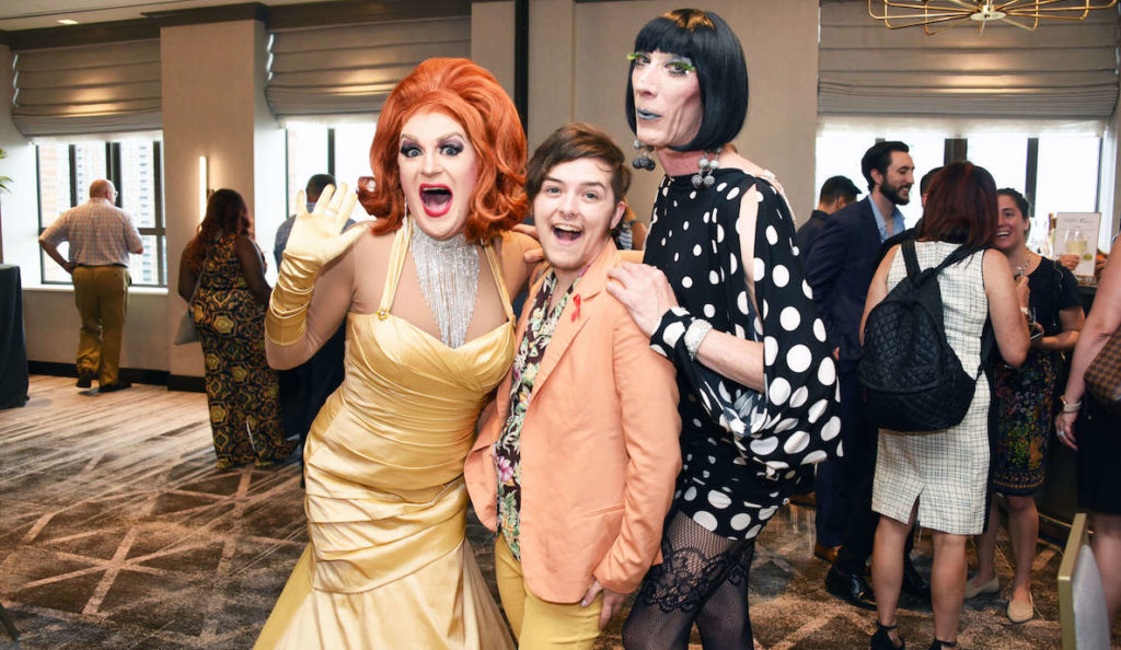 Two kooky drag queens greet a well-dressed guest at Action Wellness's annual Glamsino Royale event.