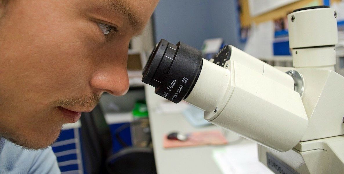 A researcher looks into a microscope, hoping to find a vaccine for the coronavirus