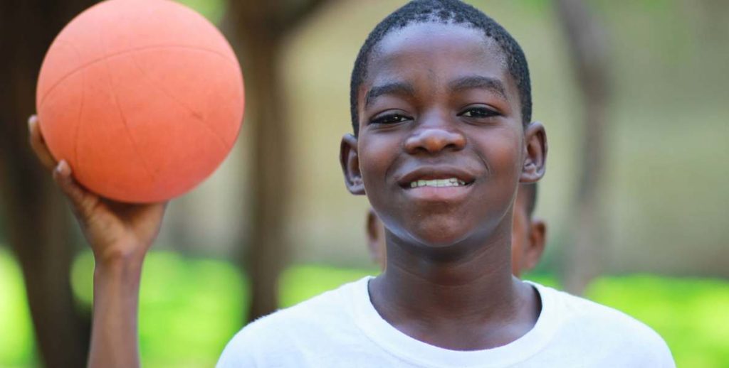 A kid holds up a basketball and stares into the camera.