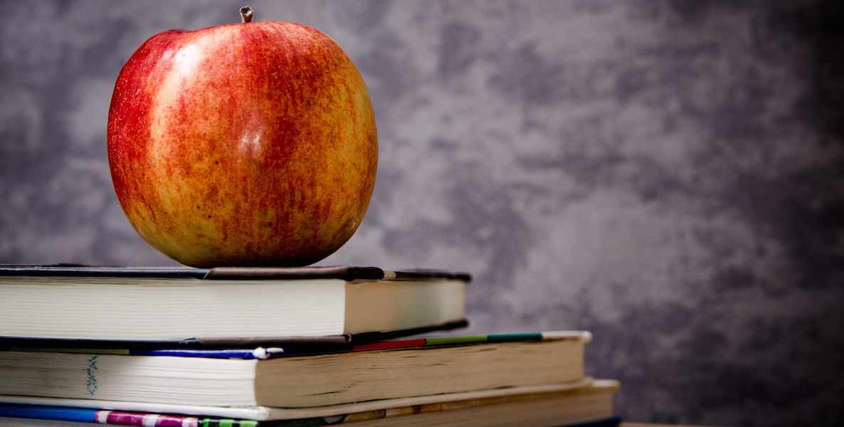 An apple sits on a stack of books.