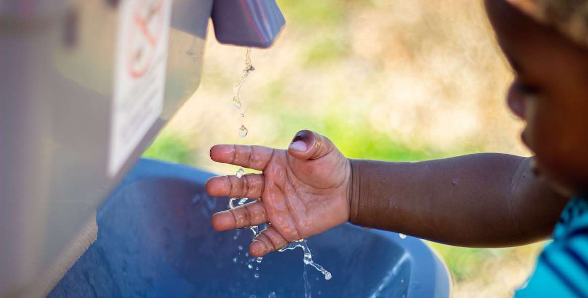 A young African American child washes his hands in a public water fountain.