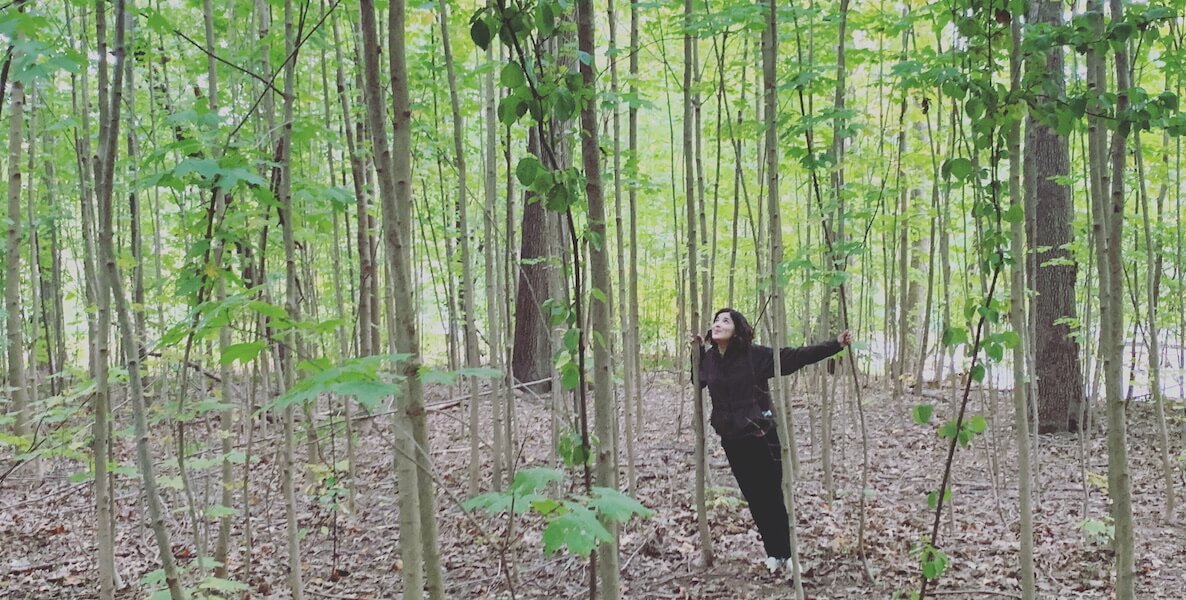 Emily's Entourage founder Emily Kramer-Golinkoff stands amongst trees in a forest.
