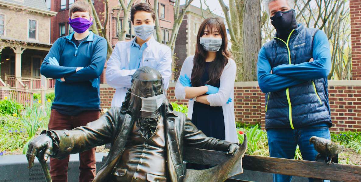 The Project Shields team poses in front of a statue of Benjamin Franklin that's wearing a face mask that they created with a 3-D printer.