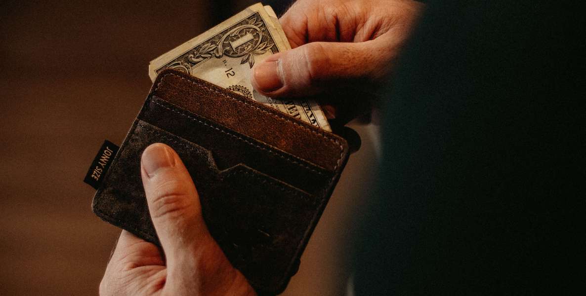 A man reaches into his wallet and pulls out a $1 bill.