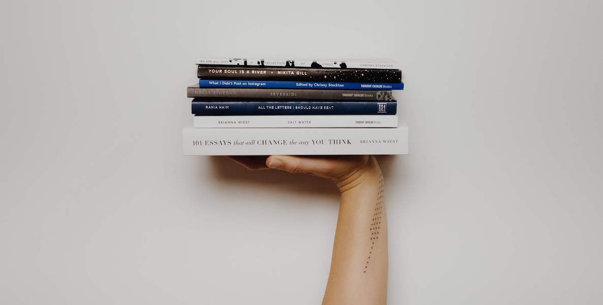 A tattooed arm holds up a stack of recommended books to read during the coronavirus quarantine