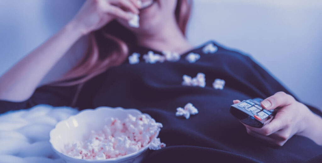 A woman lays back and watches a funny movie during her coronavirus quarantine—with popcorn in hand!